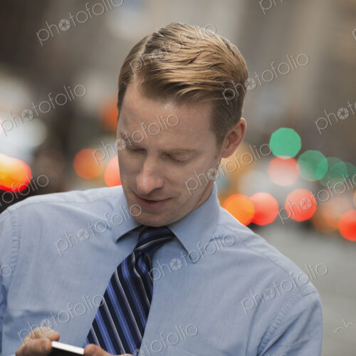 A man in a shirt and tie checking his cell phone, standing on a busy street. A man in a shirt and tie checking his cell phone, standing on a busy street.