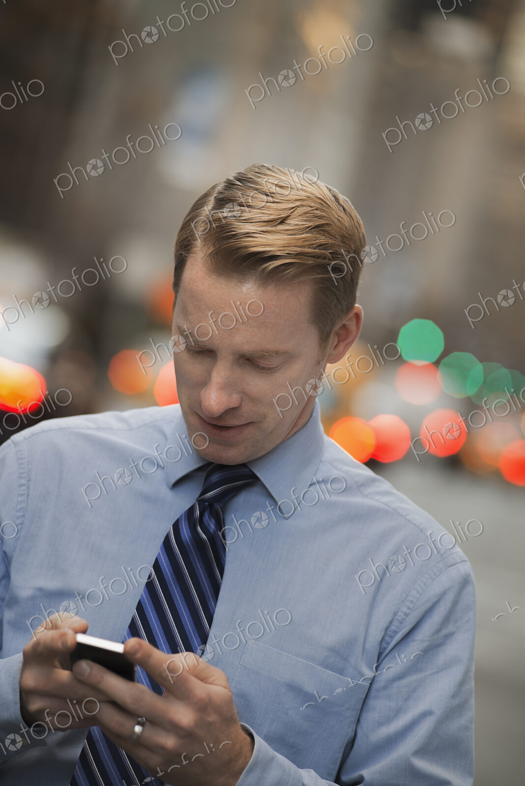 A man in a shirt and tie checking his cell phone, standing on a busy street.