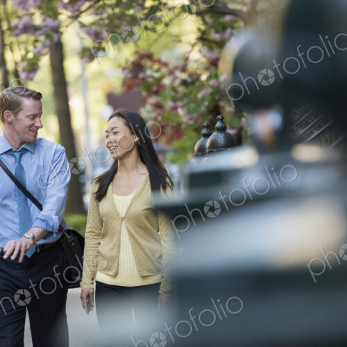 A man in a shirt and tie pushing a bicycle, and talking to a woman. A park in the city. A man in a shirt and tie pushing a bicycle, and talking to a woman. A park in the city.