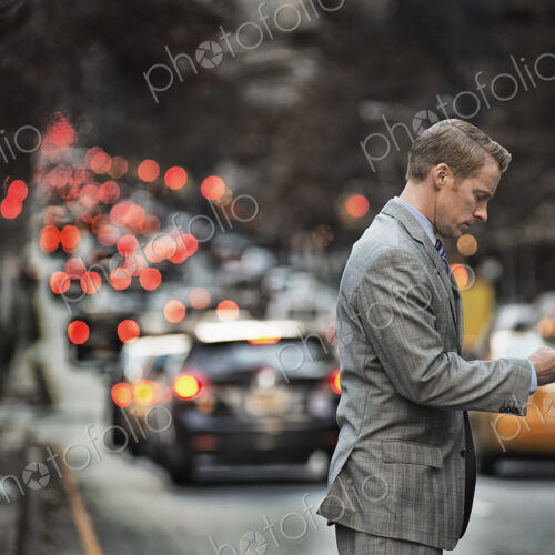 A man in a suit checking his cell phone, standing on a busy street at dusk. A man in a suit checking his cell phone, standing on a busy street at dusk.