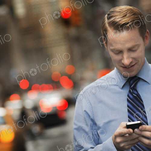 A man in a suit checking his cell phone, standing on a city sidewalk at dusk. A man in a suit checking his cell phone, standing on a city sidewalk at dusk.