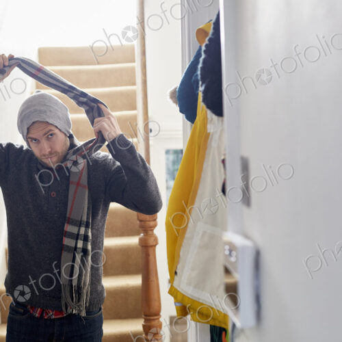 A man in a winter coat, hat and scarf arriving home, taking his scarf off. A man in a winter coat, hat and scarf arriving home, taking his scarf off.