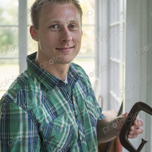 A man in a workshop, holding a carpenter's clamp in his hand.