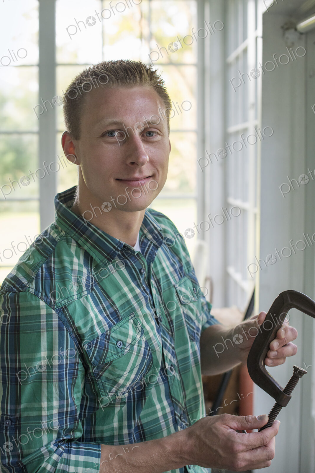 A man in a workshop, holding a carpenter’s clamp in his hand.