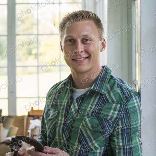 A man in a workshop, holding a carpenter's clamp in his hand.