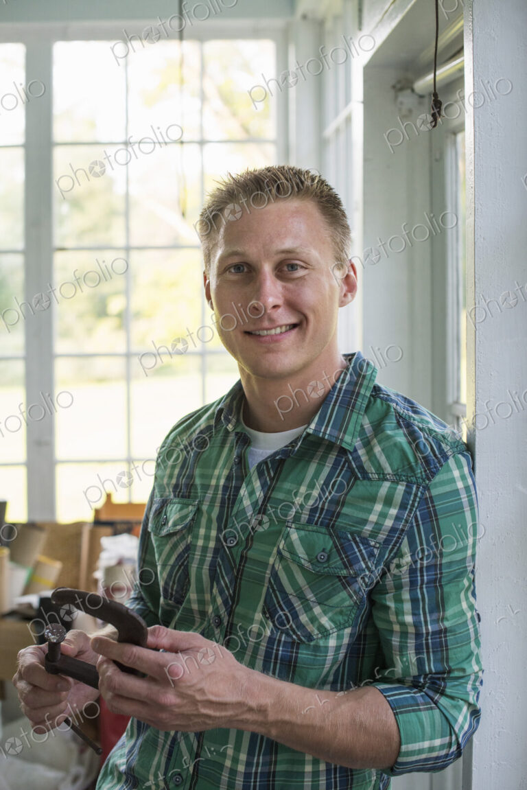 A man in a workshop, holding a carpenter's clamp in his hand.