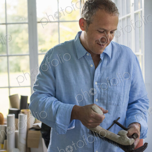A man in a workshop, holding a carpenter's clamp in his hand.