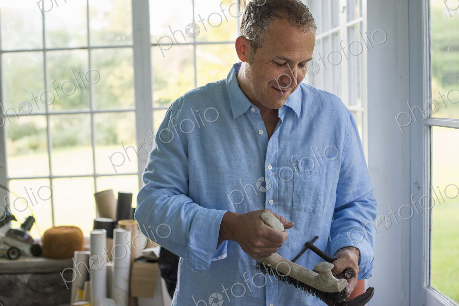 A man in a workshop, holding a carpenter’s clamp in his hand.