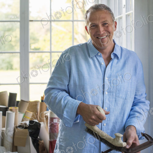 A man in a workshop, holding a carpenter's clamp in his hand.