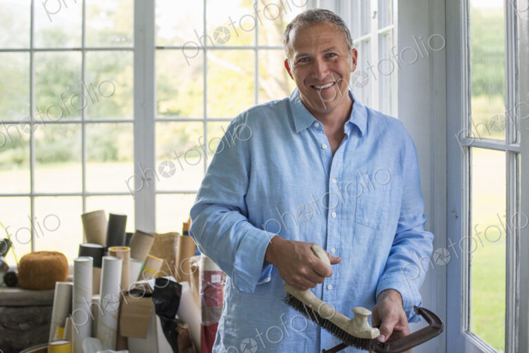 A man in a workshop, holding a carpenter's clamp in his hand.
