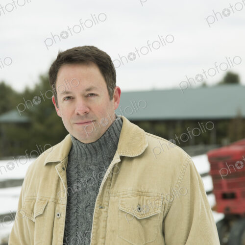 A man in jacket and jumper outside a barn building in snow. A man in jacket and jumper outside a barn building in snow.