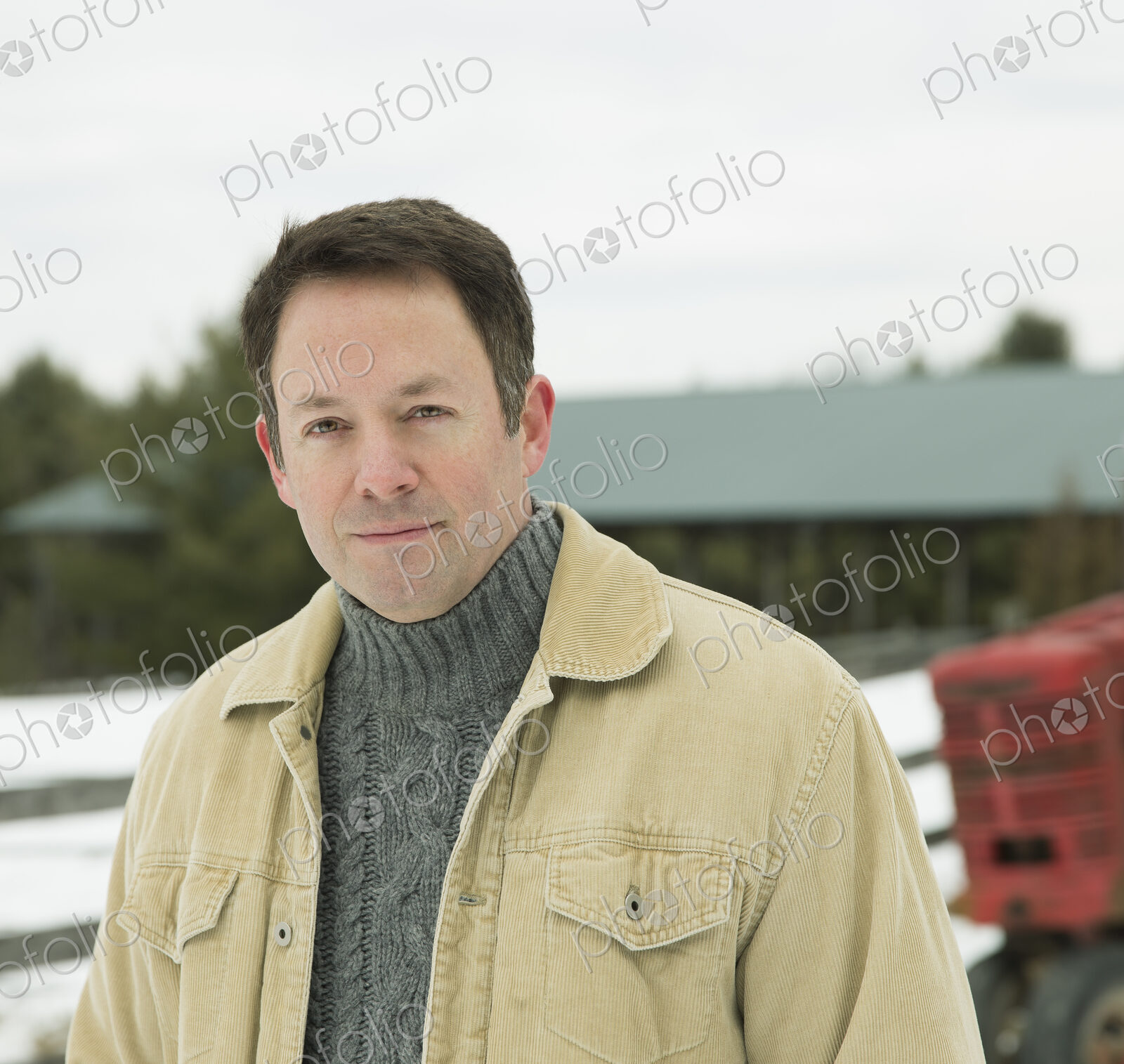 A man in jacket and jumper outside a barn building in snow.