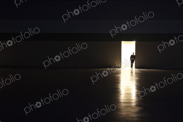 A man in silhouette standing in the doorway of a large convention center arena.