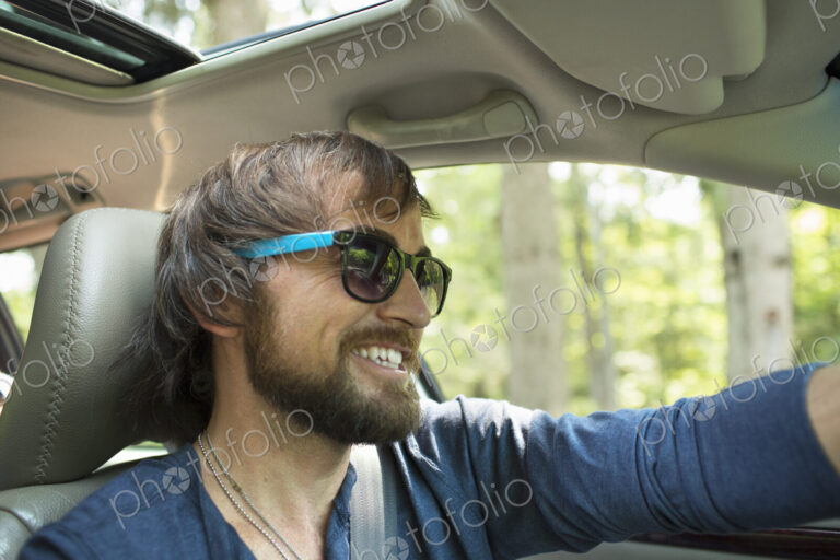A man in sunglasses in the driving seat of a car.