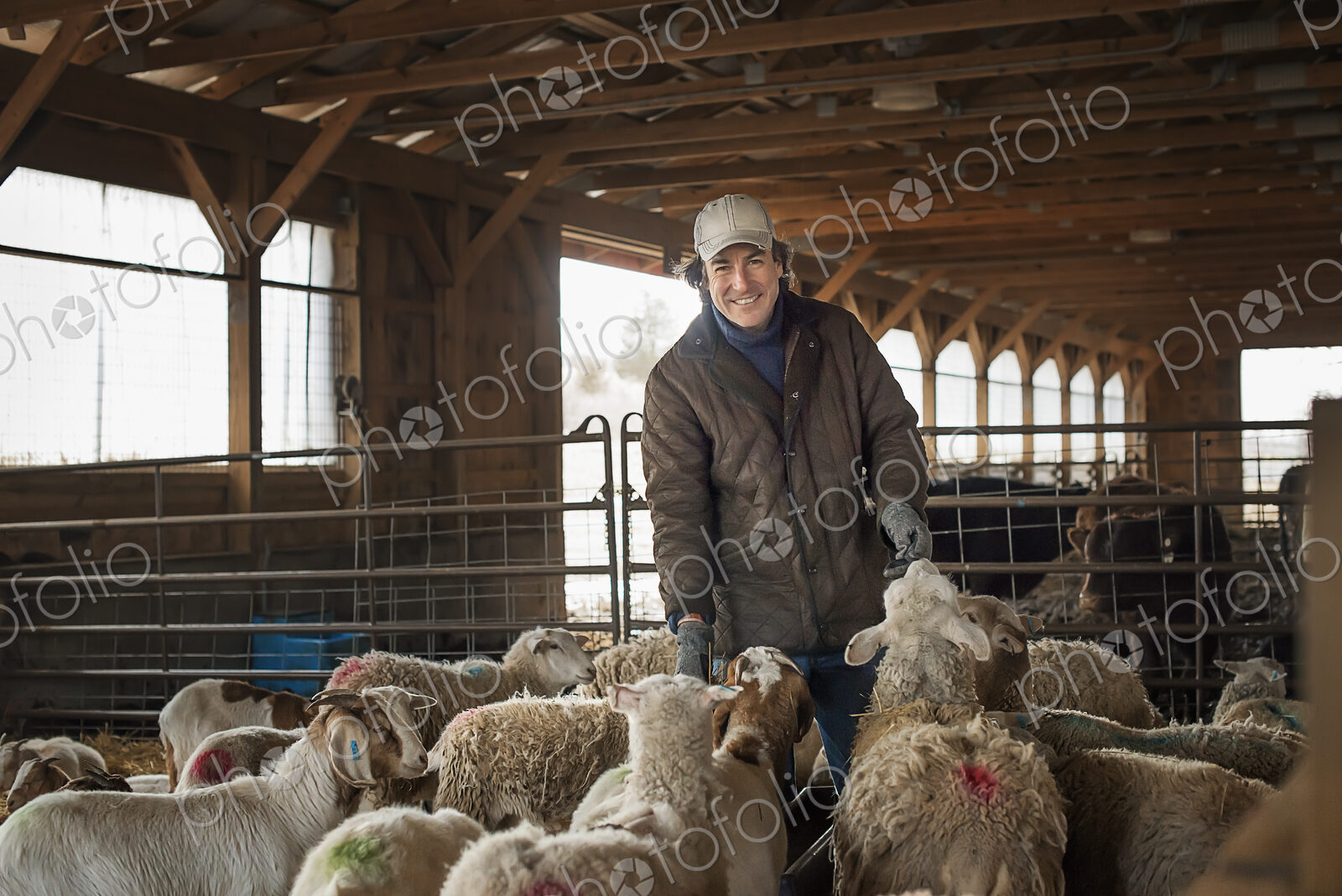 A man in the livestock pen under cover, surrounded by goats.