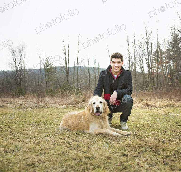 A man in the open air, on a winter day. Stroking a golden retriever dog.