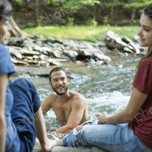 A man in the river, and two women seated on the river bank. A man in the river, and two women seated on the river bank.