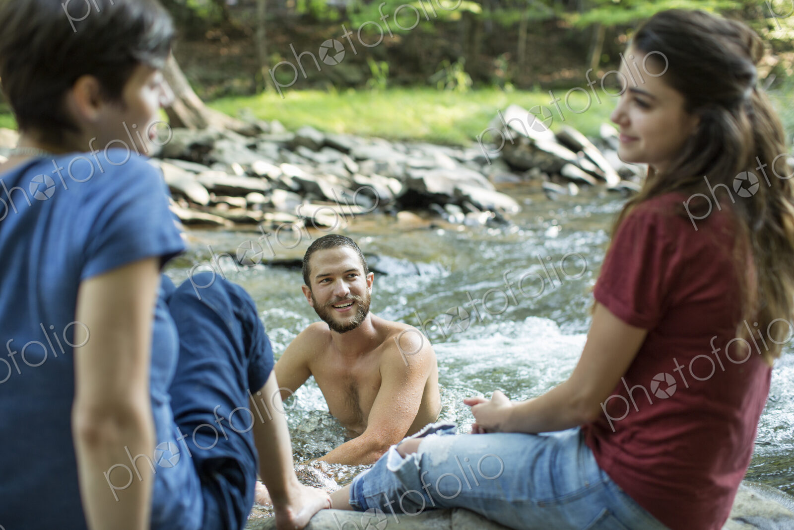 A man in the river, and two women seated on the river bank.
