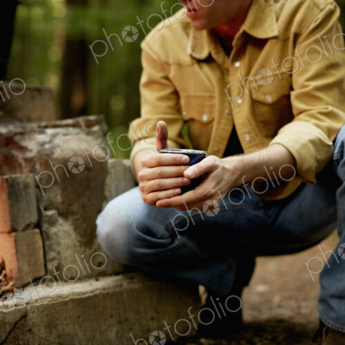 A man kneeling by a blazing camp fire.