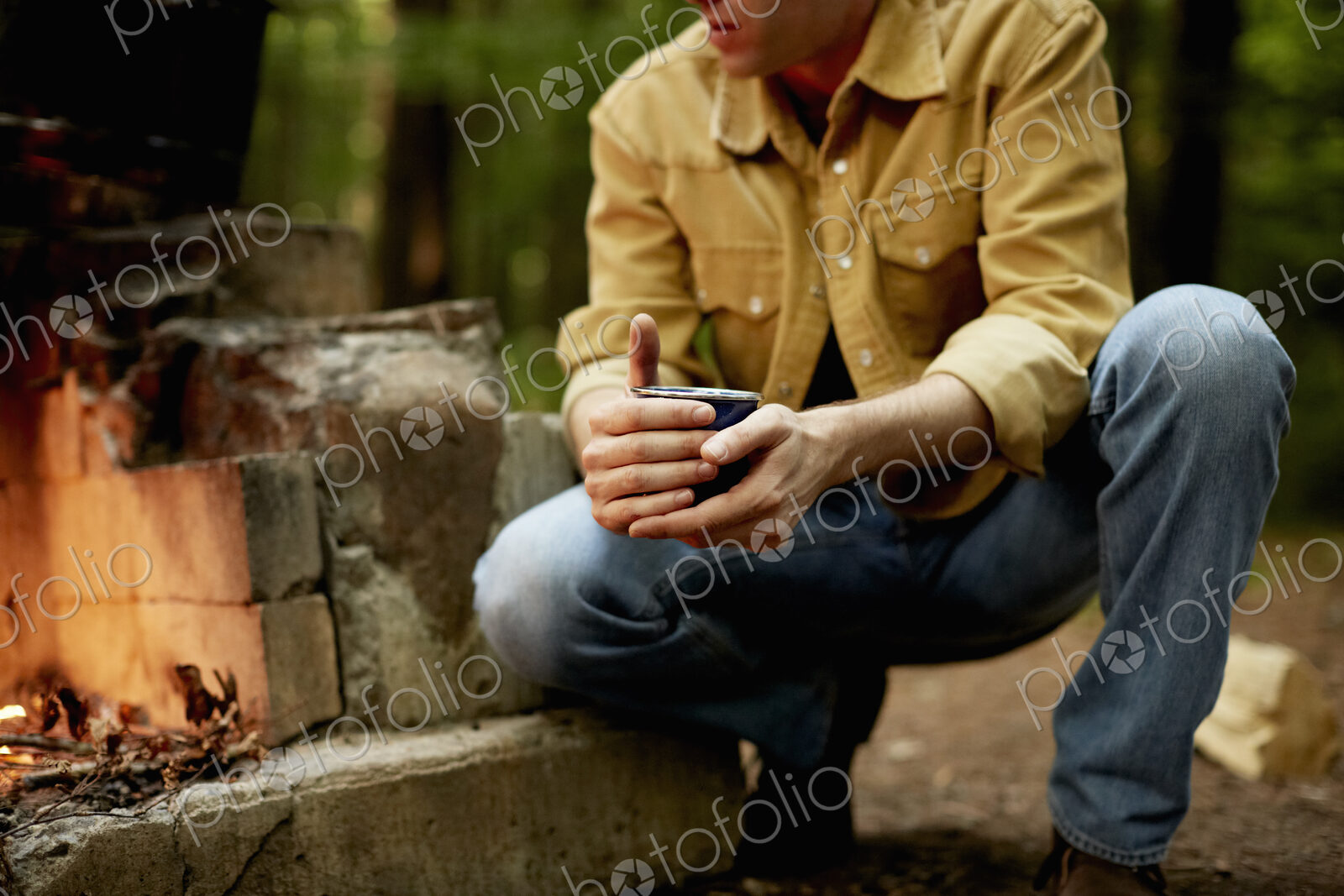A man kneeling by a blazing camp fire.