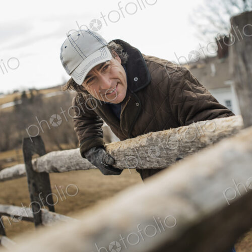 A man leaning against a post and rail fence on a farm in winter. A man leaning against a post and rail fence on a farm in winter.