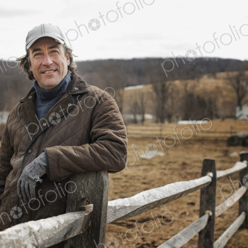 A man leaning against a post and rail fence on a farm in winter. A man leaning against a post and rail fence on a farm in winter.
