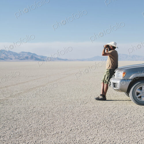 A man leaning against a truck, looking through binoculars. A man leaning against a truck, looking through binoculars.
