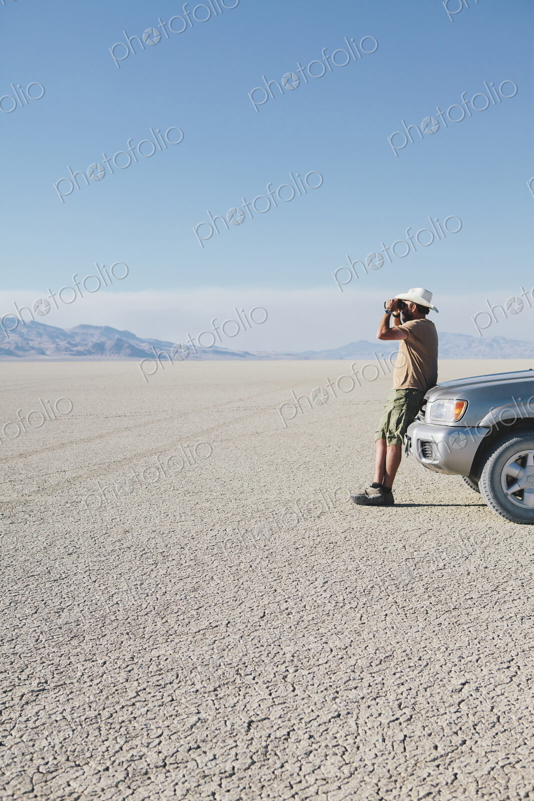 A man leaning against a truck, looking through binoculars.