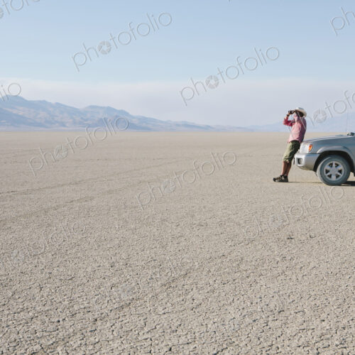A man leaning against a truck, looking through binoculars. A man leaning against a truck, looking through binoculars.