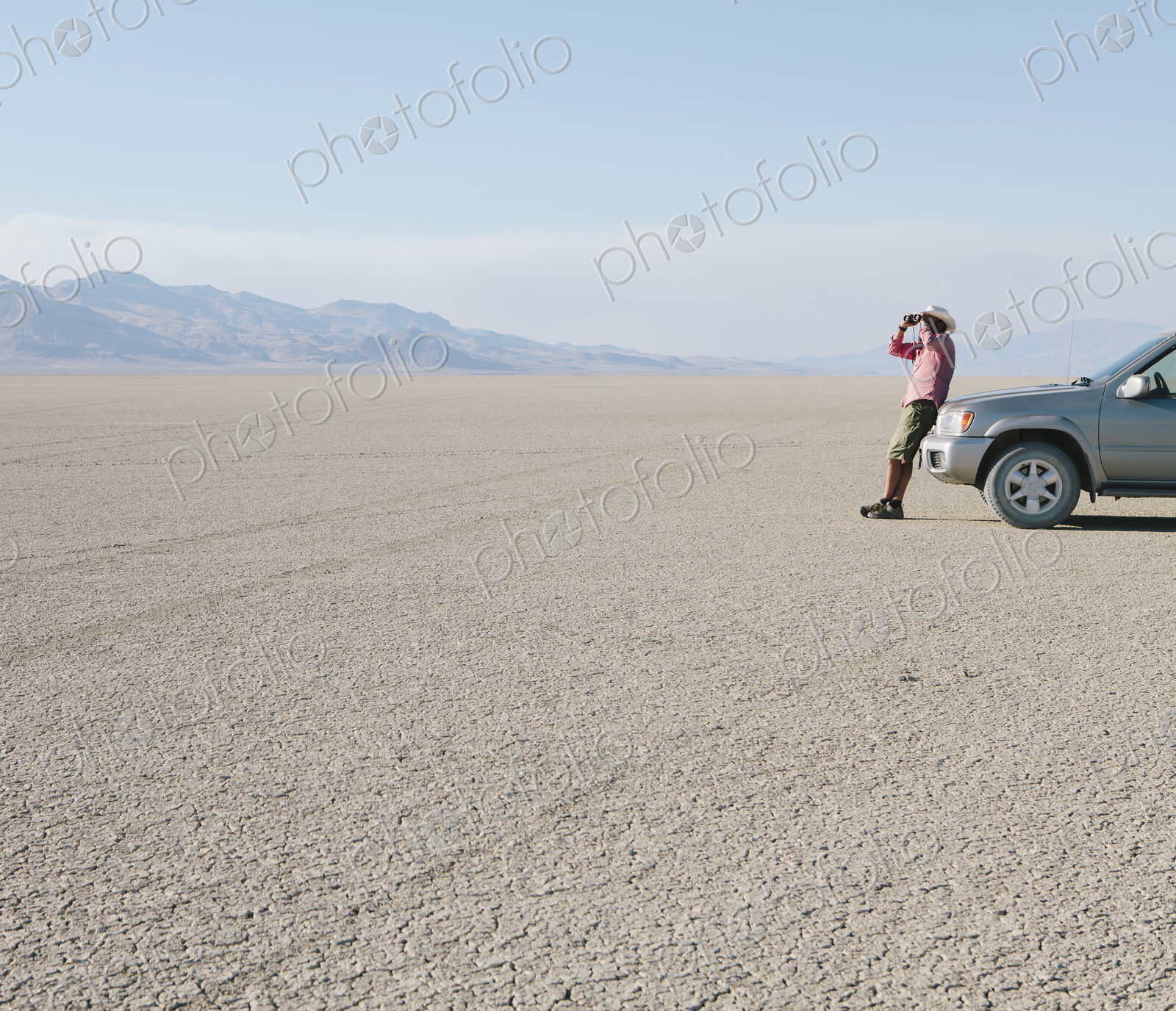 A man leaning against a truck, looking through binoculars.