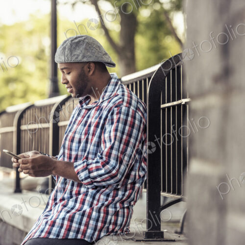 A man leaning on a railing, looking at a smart phone A man leaning on a railing, looking at a smart phone