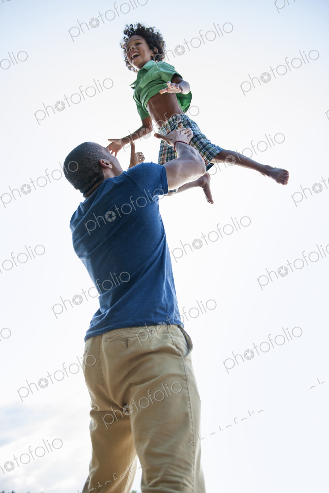 A man lifting a small boy up above his head in play.