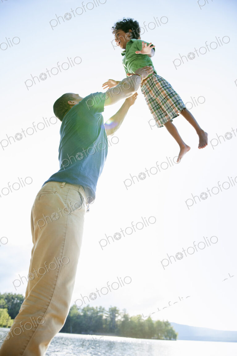 A man lifting a small boy up above his head in play.