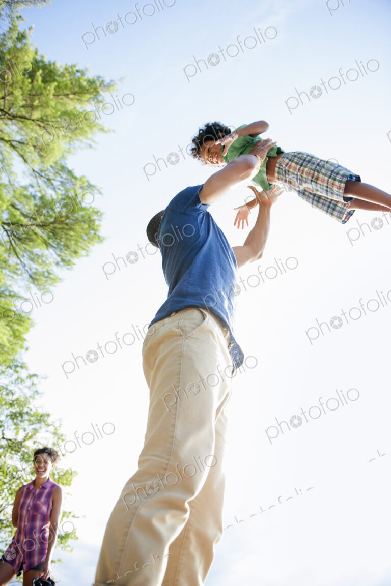 A man lifting a small boy up above his head in play.