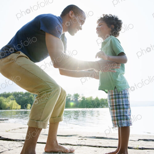 A man lifting a small boy up, playing in the sun by a lake. A man lifting a small boy up, playing in the sun by a lake.