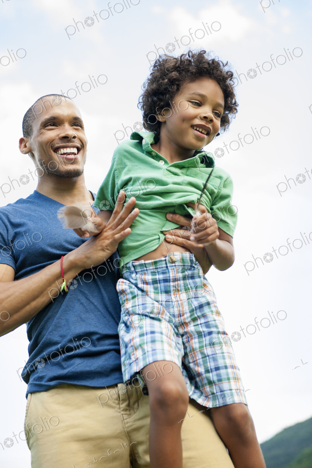 A man lifting his son up in his arms, playing outdoors.
