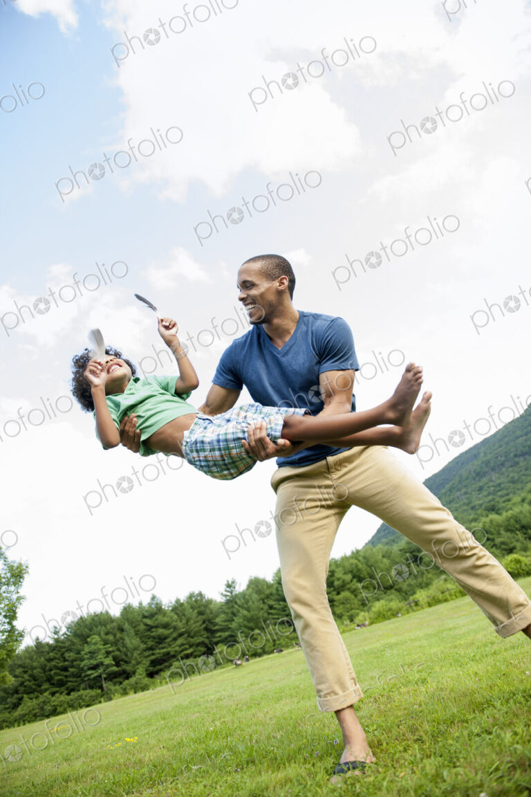 A man lifting his son up in his arms, playing outdoors.