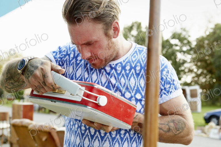 A man looking at a red vintage radio at a flea market.