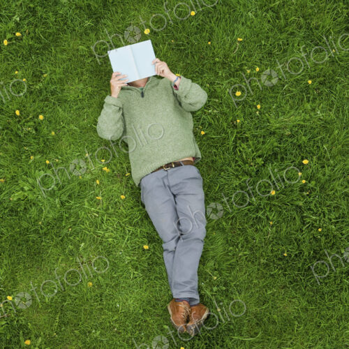 A man lying on his back on the grass, reading a book. A man lying on his back on the grass, reading a book.