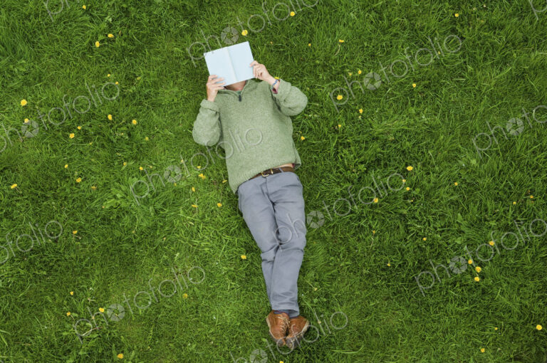 A man lying on his back on the grass, reading a book.