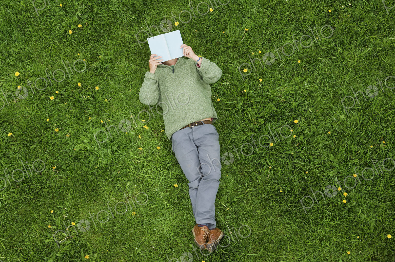 A man lying on his back on the grass, reading a book.