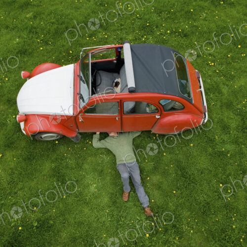 A man lying on his back under a red car, inspecting the underside of the car. A man lying on his back under a red car, inspecting the underside of the car.