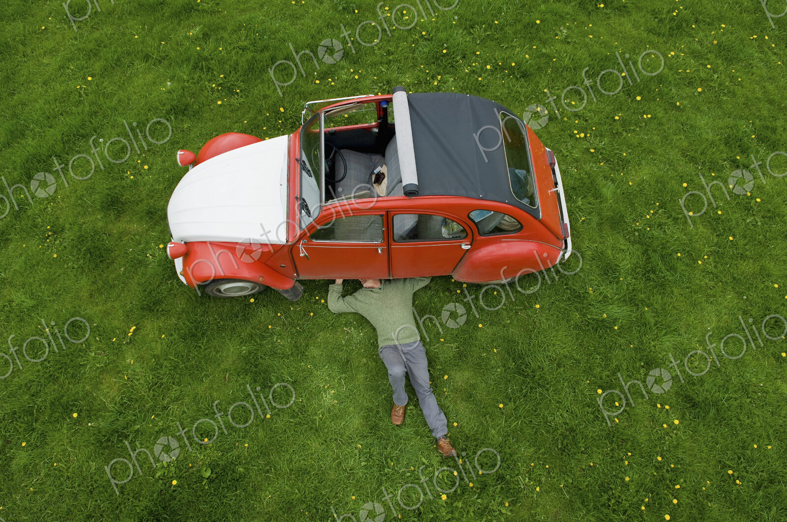 A man lying on his back under a red car, inspecting the underside of the car.