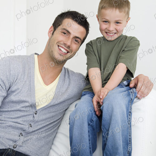 A man on a sofa beside a young boy wearing jeans. A man on a sofa beside a young boy wearing jeans.