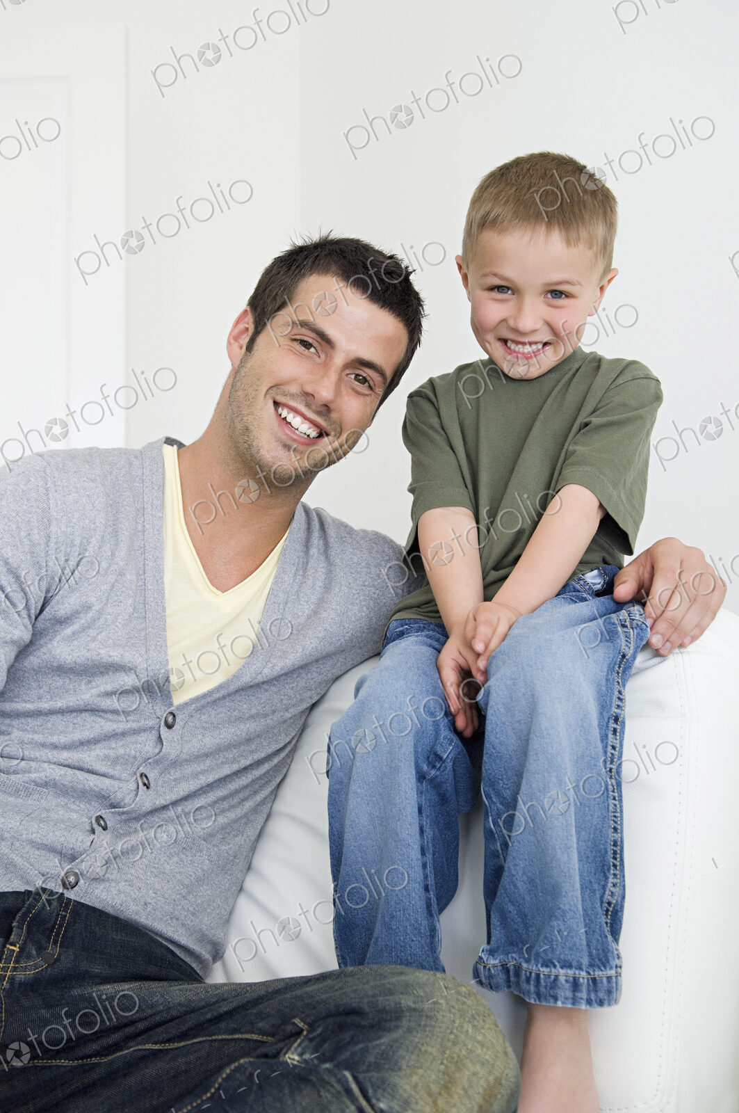 A man on a sofa beside a young boy wearing jeans.