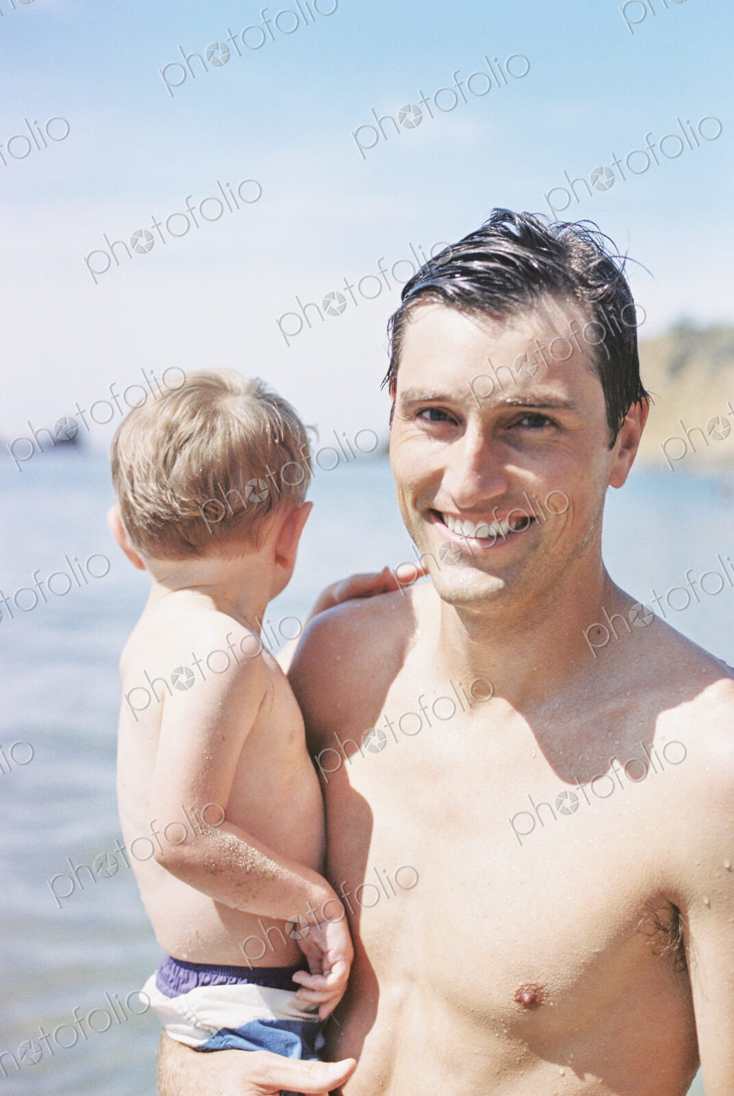 A man on the beach, smiling, carrying his young son