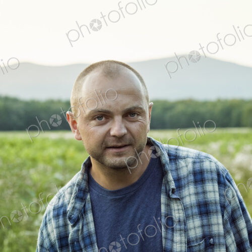A man outdoors in a wild flower meadow wearing a checked shirt. A man outdoors in a wild flower meadow wearing a checked shirt.