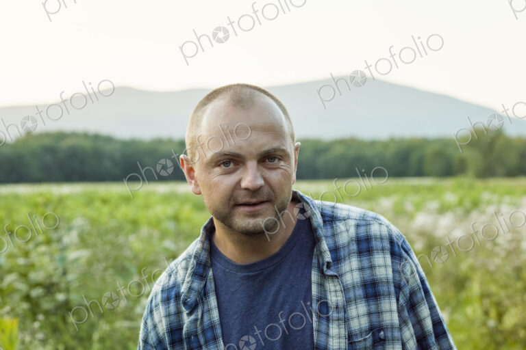 A man outdoors in a wild flower meadow wearing a checked shirt.
