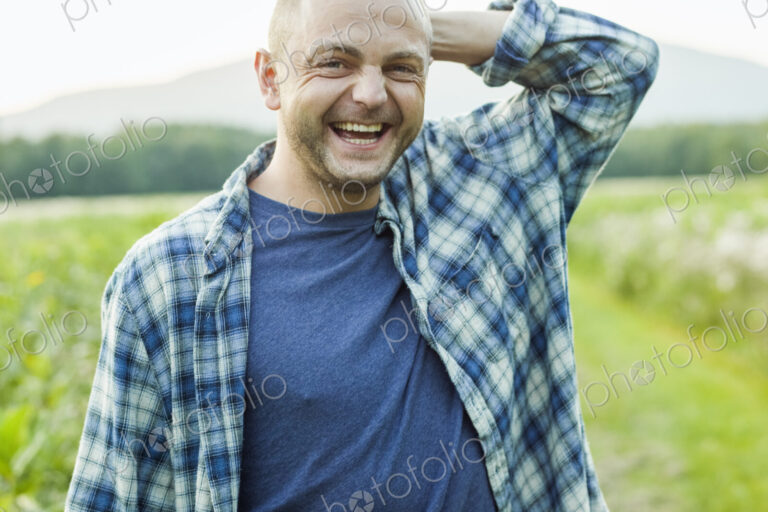 A man outdoors in a wild flower meadow wearing a checked shirt.