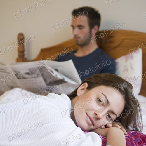A man reading the paper in bed, and a woman relaxing smiling. A man reading the paper in bed, and a woman relaxing smiling.